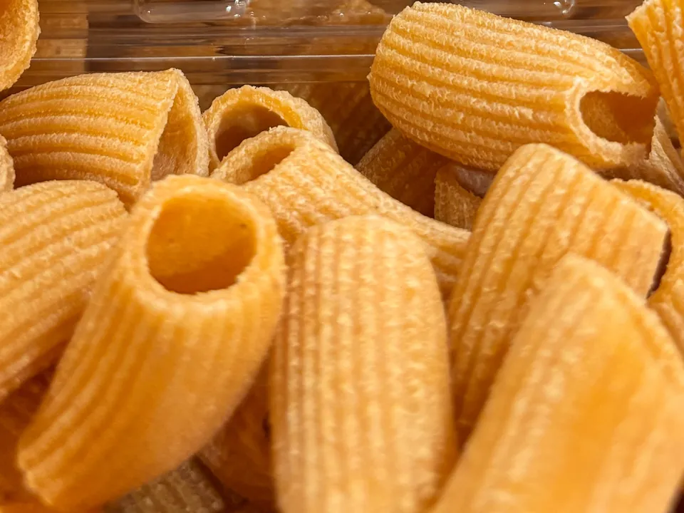 Close-up of fresh carrot rigatoni, orange ridged tubes piled together.