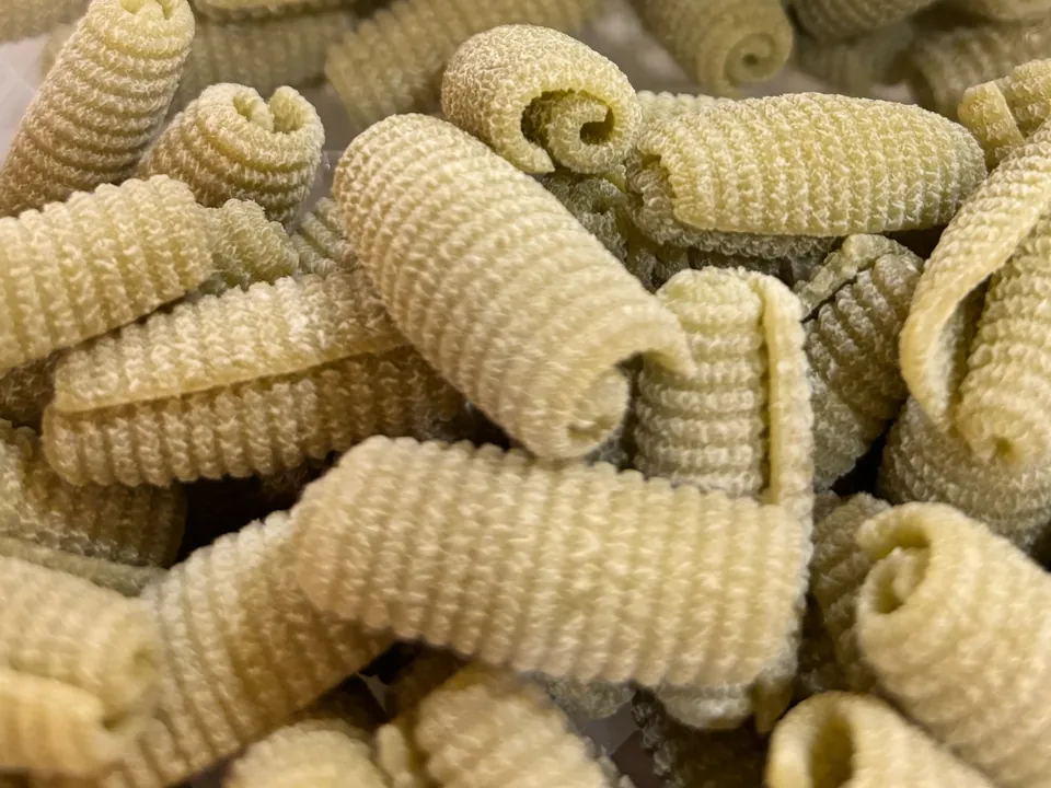 Close-up of fresh spinach gnocchi, pale green ridged shells with curled edges.